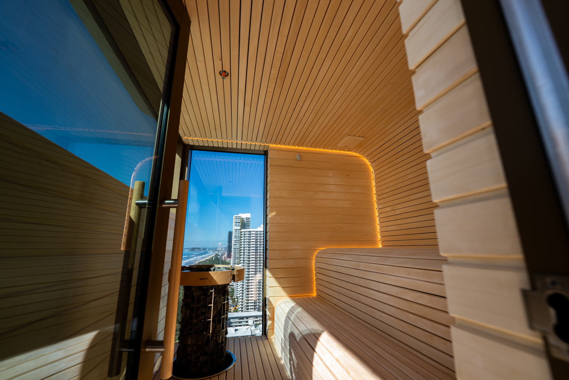 Light timber sauna interior with curved illuminated bench and glazed outlook