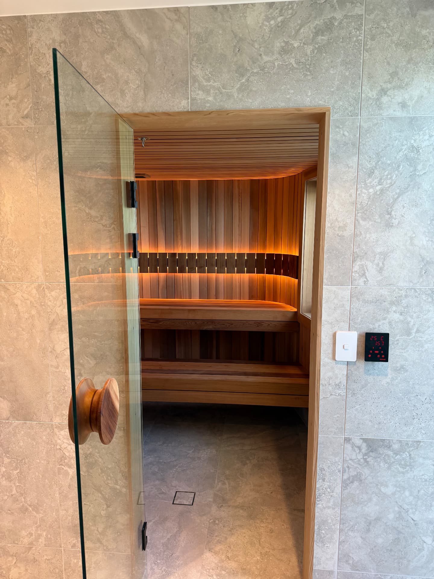 Glass sauna door framed by natural stone with illuminated timber benches