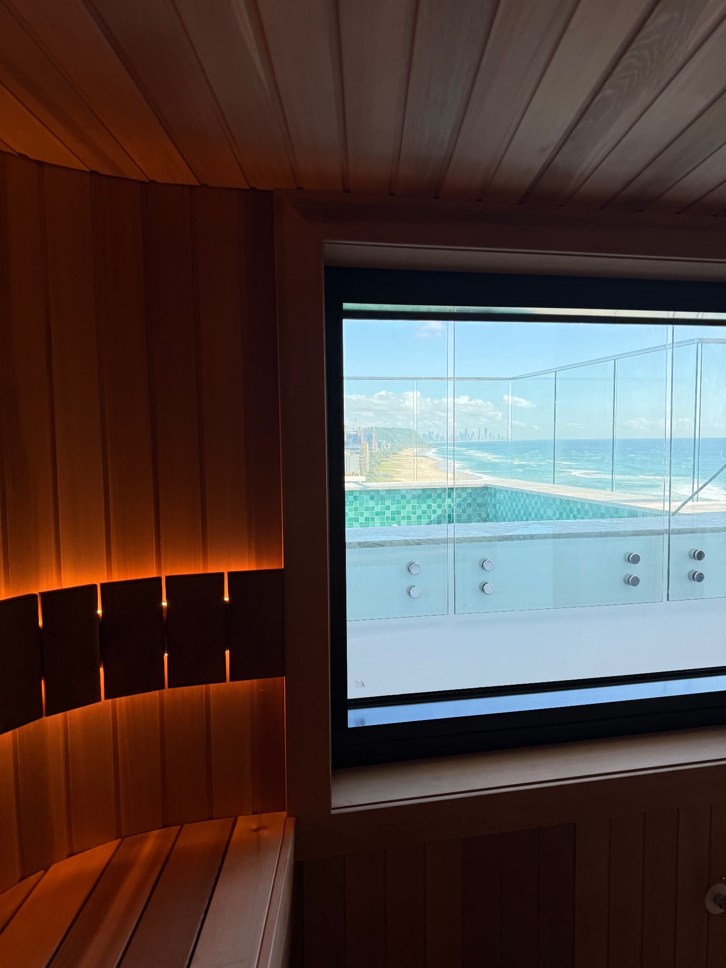 Warm timber sauna interior with a window overlooking a swimming pool